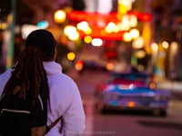 a man with dreadlocks walking down a street at night